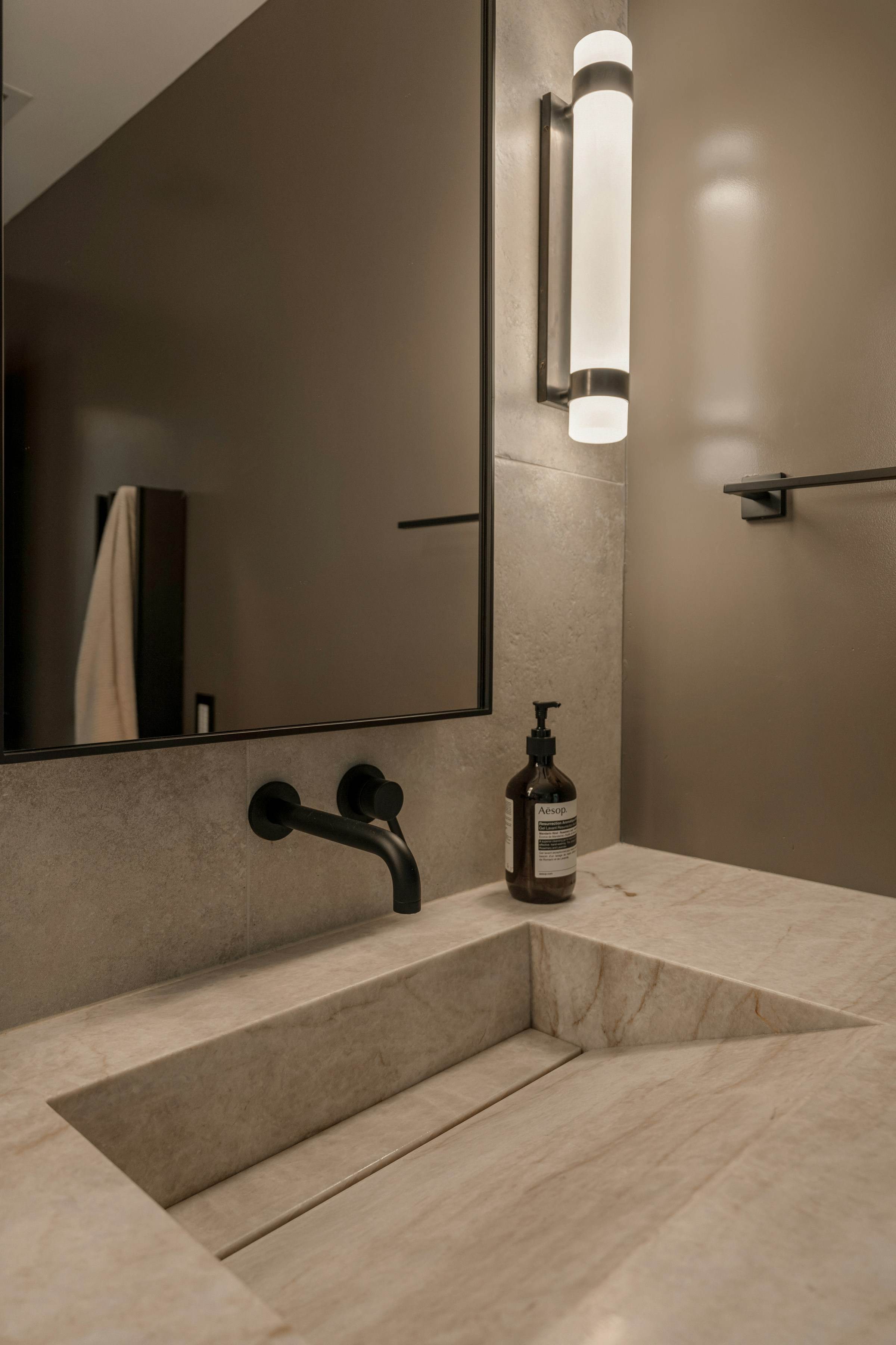 Integrated stone basin with a wall-mounted matte black tap and slim wall light