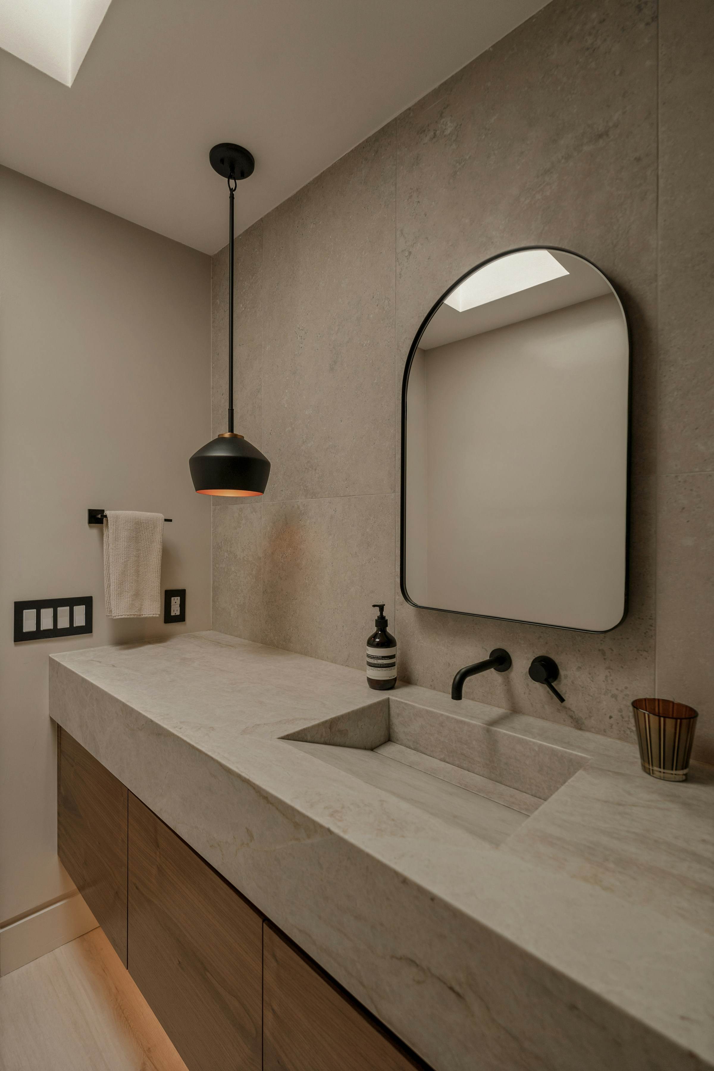 Stone vanity with integrated basin, arched mirror and black pendant