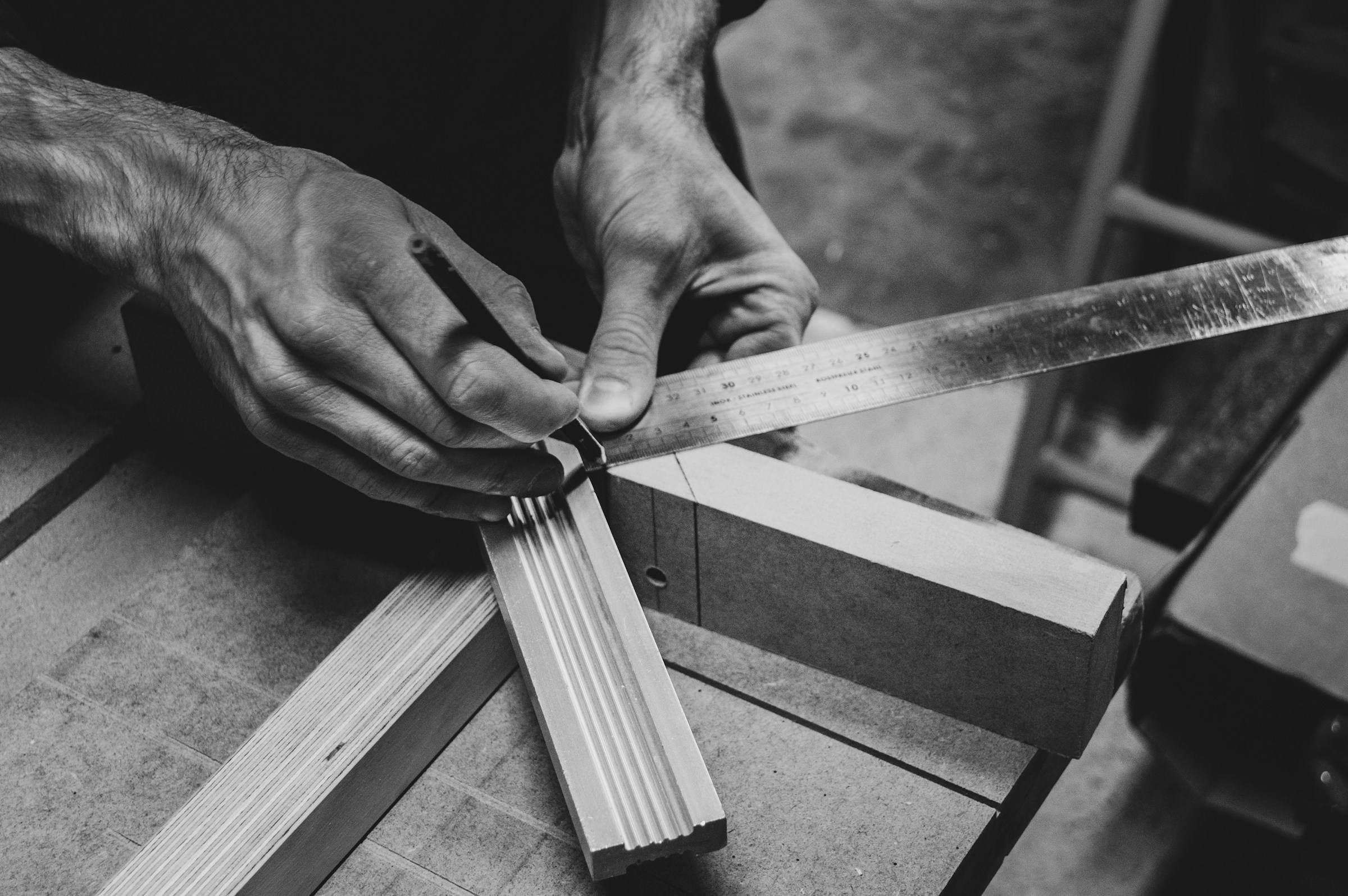 Black-and-white photo of hands marking timber with a steel square