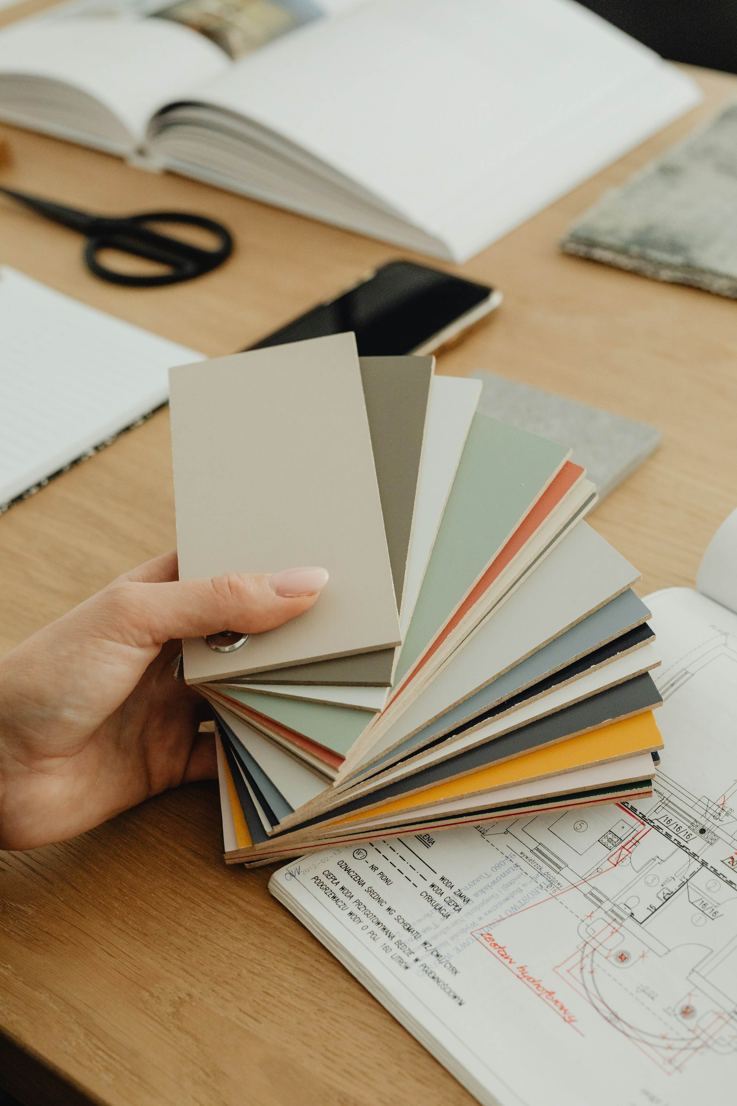 Hand holding a fan of paint colour swatches over a drawing