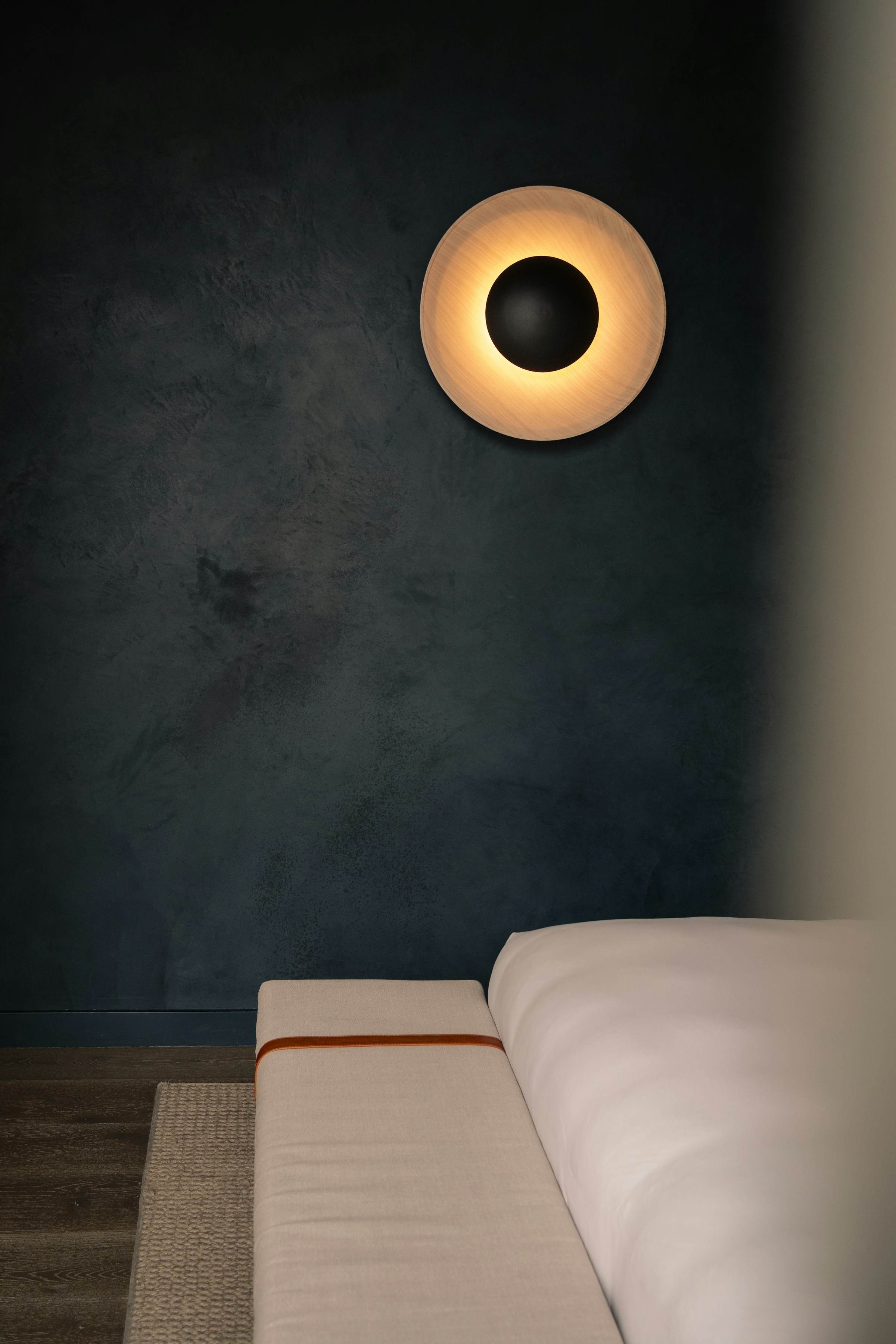 Round wall sconce glowing on a dark plaster wall above a sofa