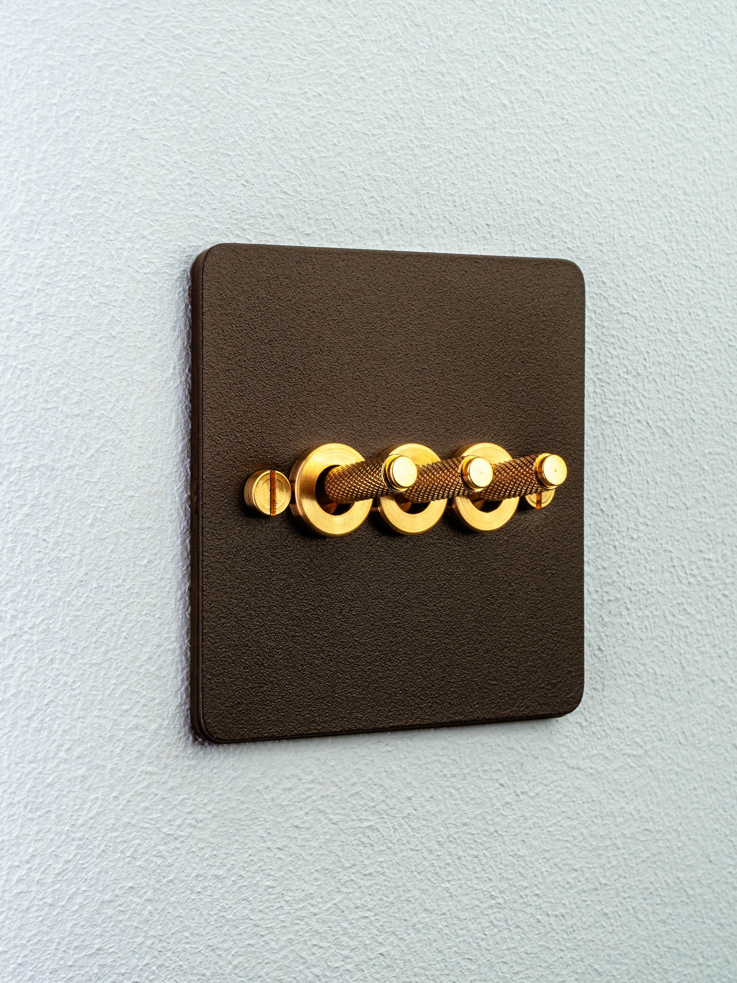 Bronze toggle light switch plate with brass toggles on a pale wall