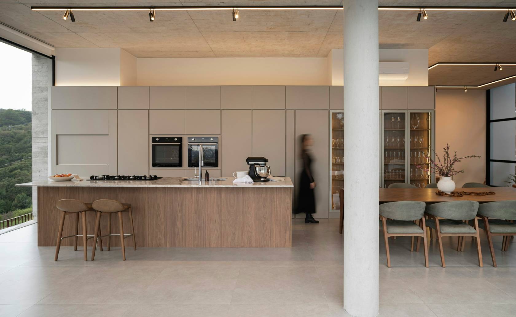 Open-plan kitchen with a walnut-clad island, stone worktop and full-height cabinetry beneath a concrete ceiling