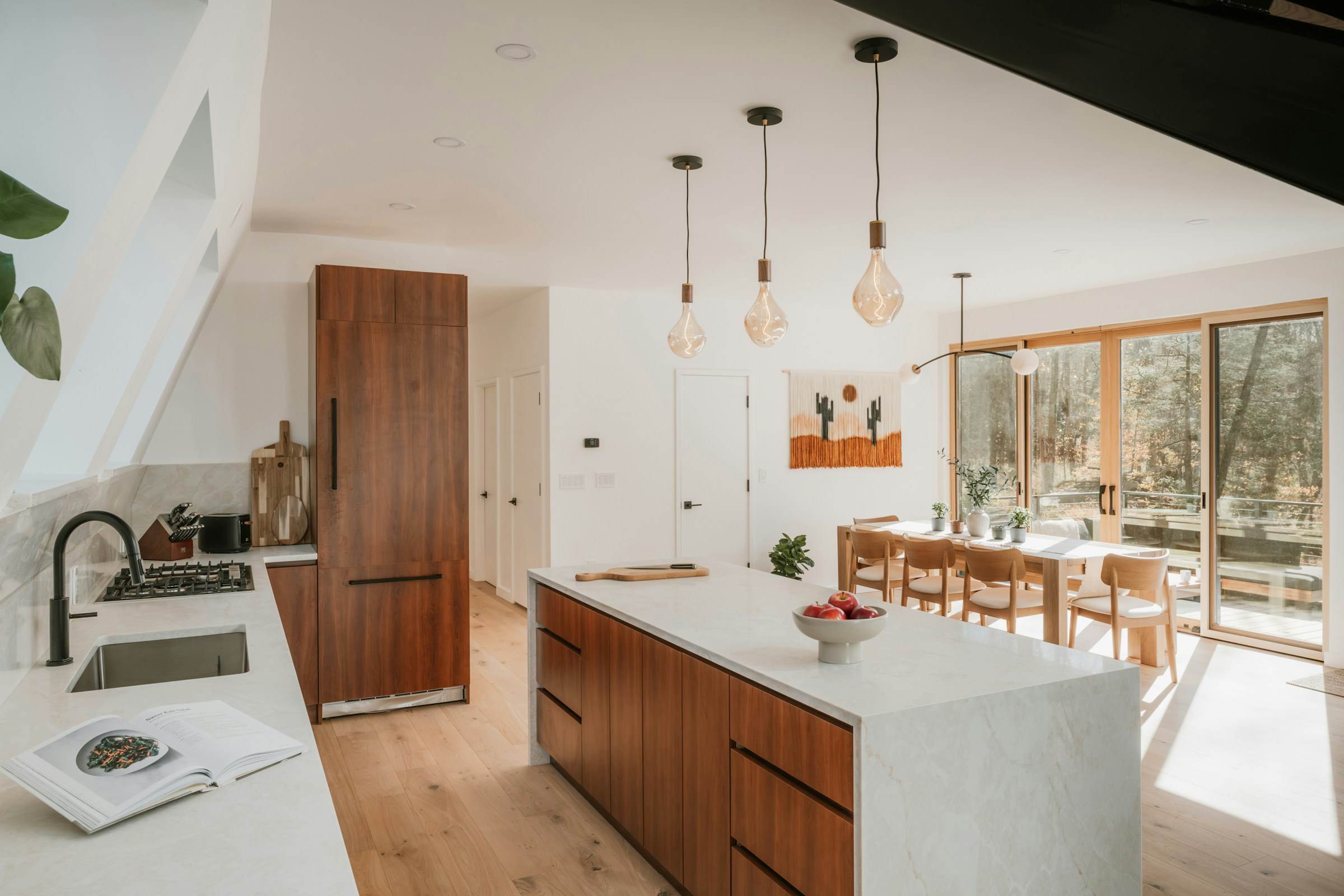Light-filled kitchen with walnut cabinetry, stone island and pendant lights