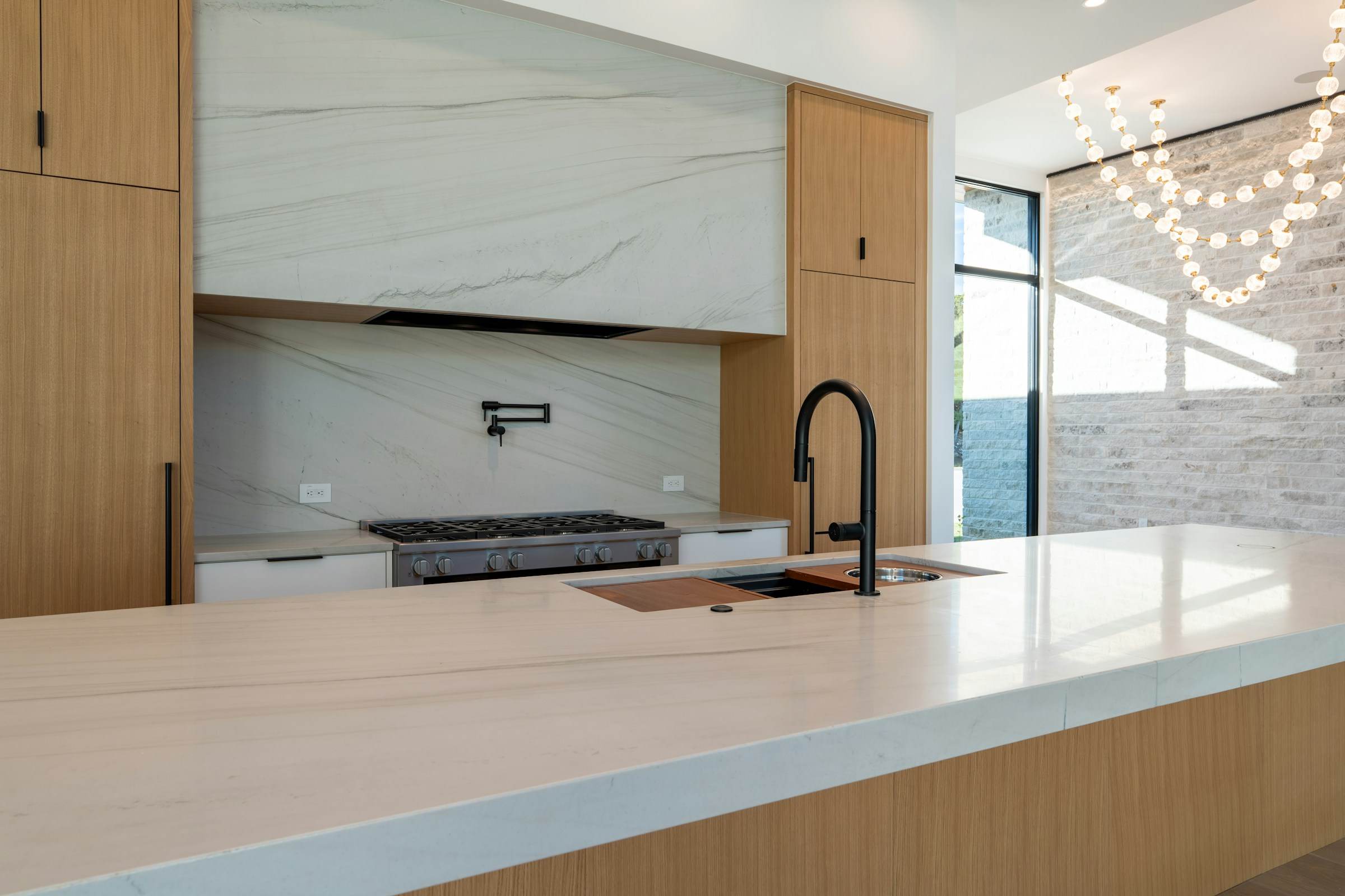 Waterfall stone island, oak tall cabinets and black fixtures in a modern kitchen