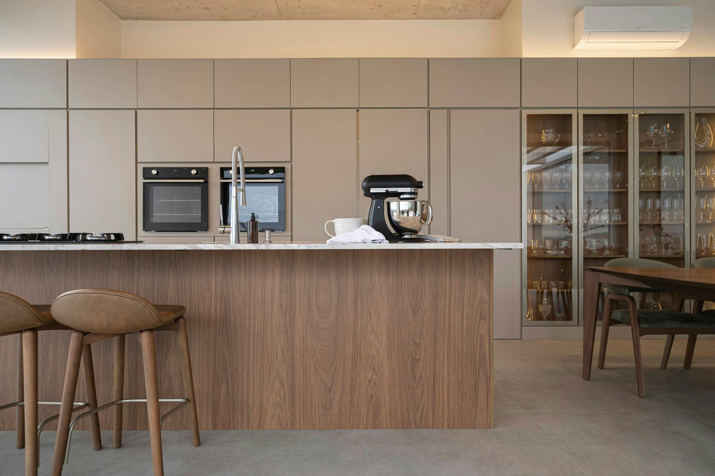 Walnut kitchen island with stone worktop in front of floor-to-ceiling handleless cabinets