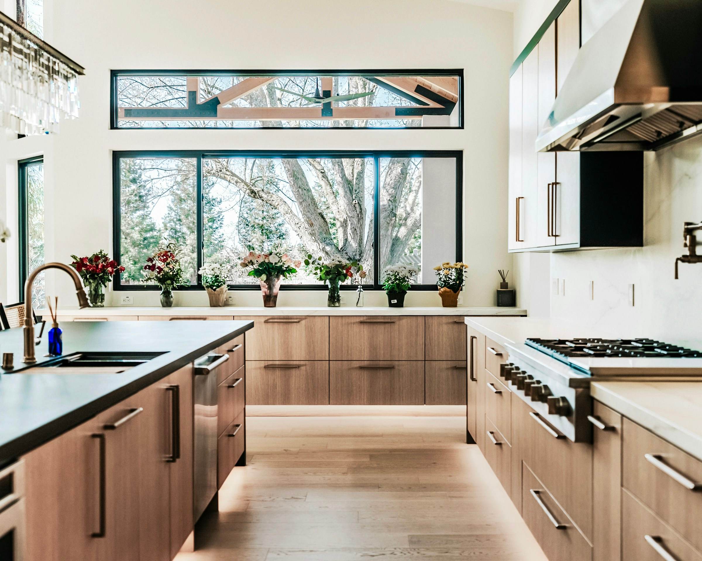 Oak kitchen cabinetry under a wide black-framed window, with brass tap and range