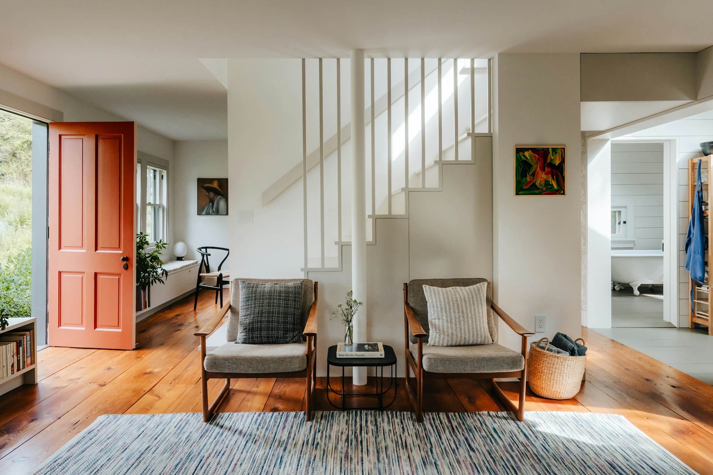 Entry hall with an open white staircase, hardwood floors and paired lounge chairs