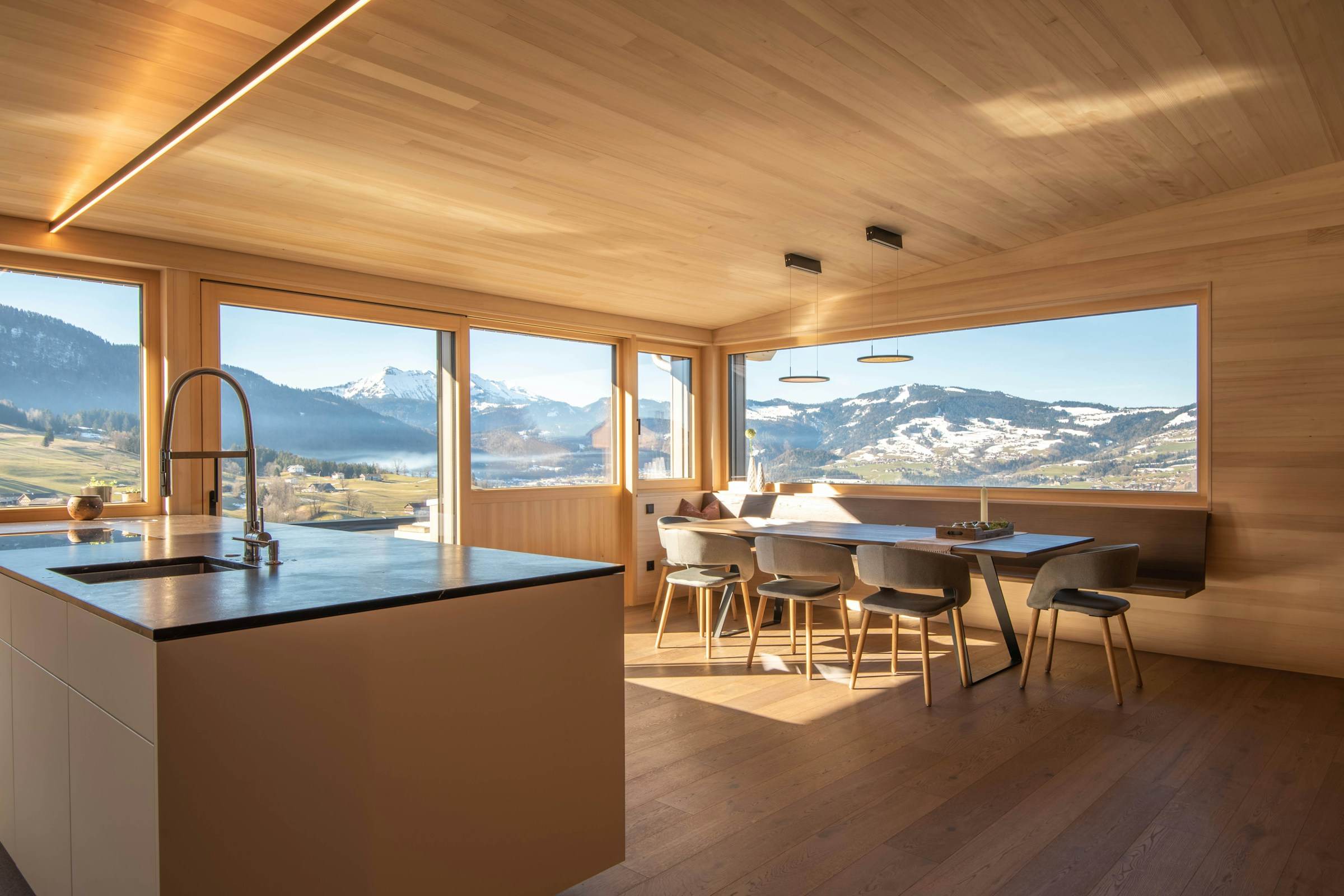 Timber-lined kitchen and dining room with linear ceiling lighting and wide picture windows